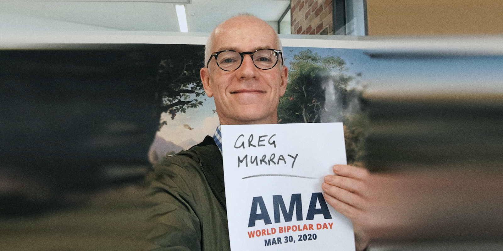 Greg sitting in an office, holding a sign proving he will be involved in the bipolar ama.