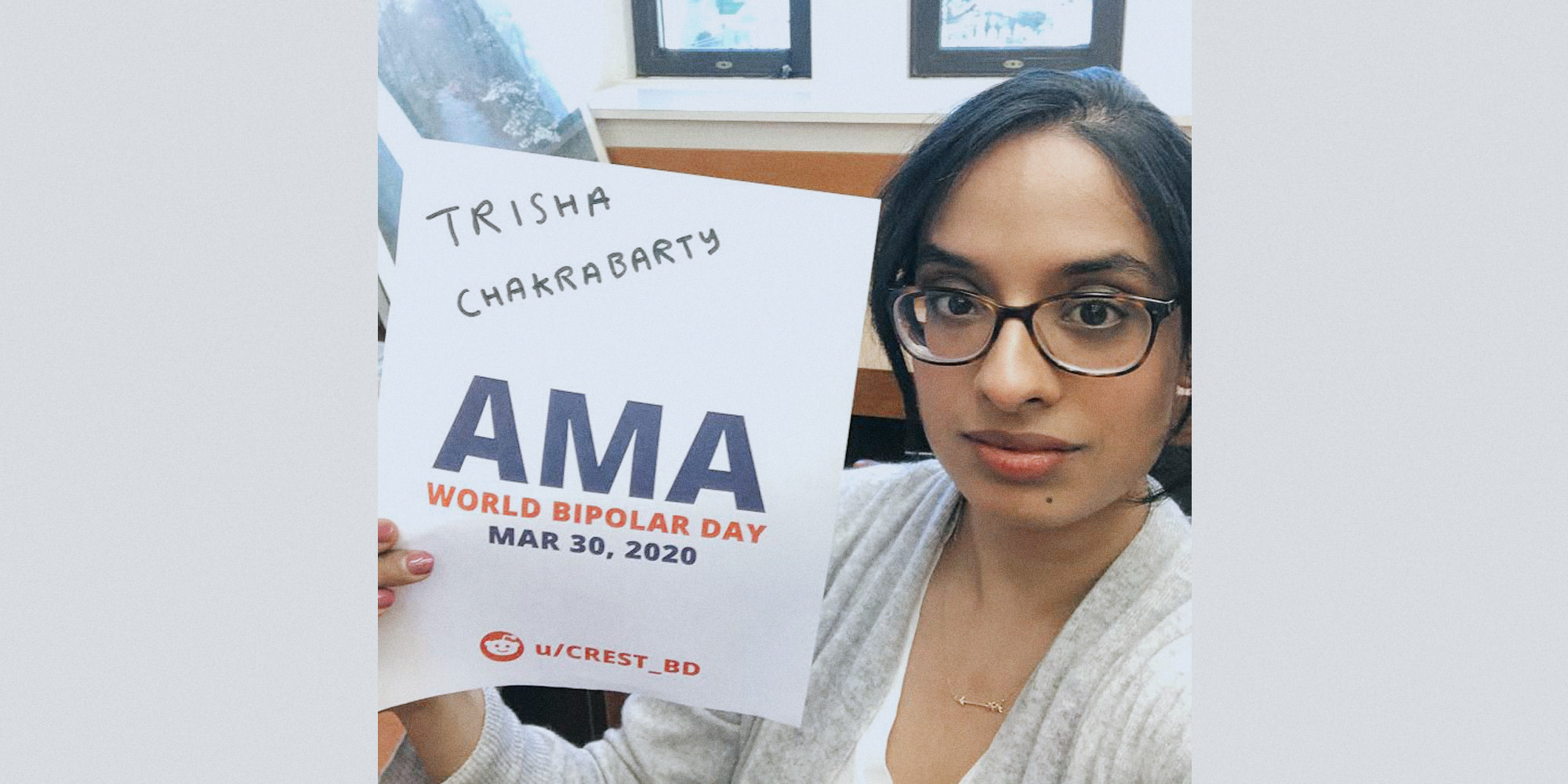 Trisha sitting in an office, looking upwards at the camera and holding a proof sign.